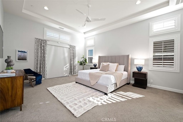 bedroom with a raised ceiling, light colored carpet, and ceiling fan