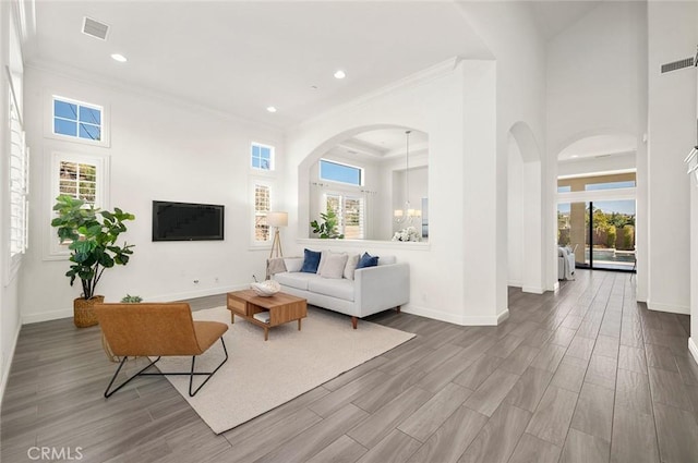 living room featuring crown molding, a towering ceiling, a healthy amount of sunlight, and a chandelier