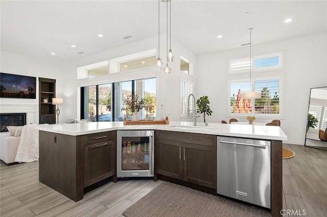 kitchen with decorative light fixtures, an island with sink, sink, beverage cooler, and stainless steel dishwasher