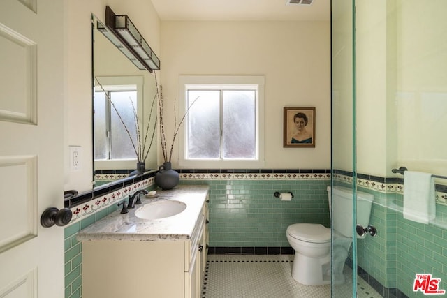 bathroom with tile patterned floors, toilet, tile walls, vanity, and a shower with door