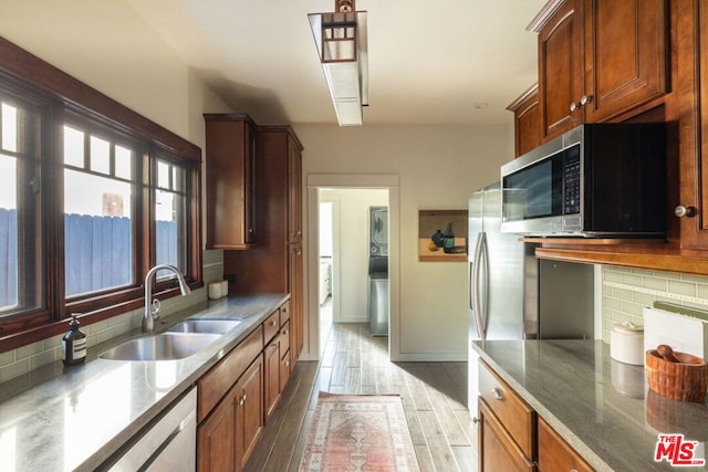 kitchen featuring stacked washing maching and dryer, sink, dark stone countertops, decorative backsplash, and stainless steel appliances