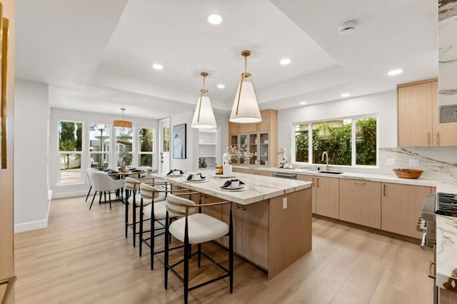 kitchen with sink, a breakfast bar area, a kitchen island, light brown cabinetry, and decorative light fixtures