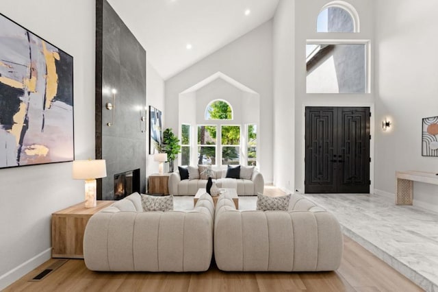 living room with high vaulted ceiling, a tile fireplace, and light wood-type flooring