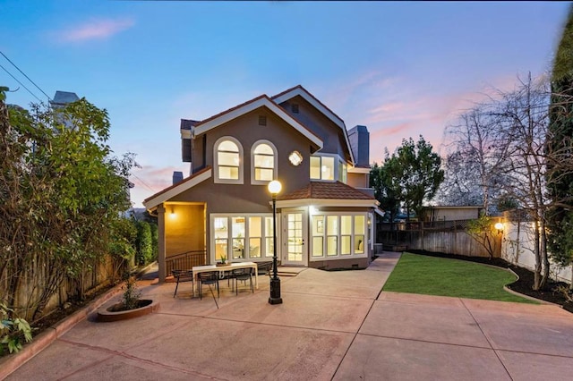 back house at dusk with a patio area and a lawn