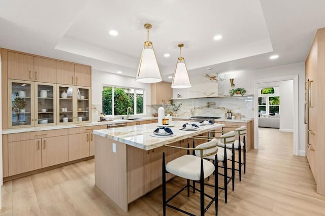 kitchen with light stone countertops, decorative light fixtures, light brown cabinetry, and a raised ceiling