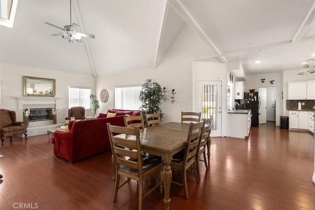 dining space featuring high vaulted ceiling, dark wood-style flooring, a fireplace, and a ceiling fan