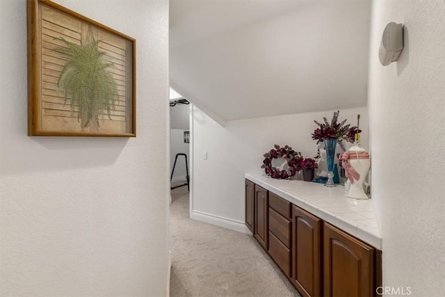 corridor with lofted ceiling, baseboards, and light colored carpet