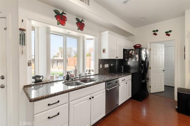 kitchen with dark wood finished floors, appliances with stainless steel finishes, white cabinetry, a sink, and dark stone countertops