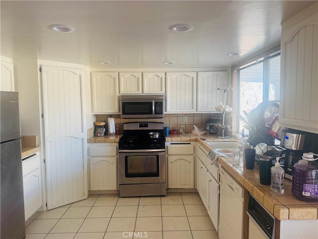 kitchen with light tile patterned floors, sink, appliances with stainless steel finishes, backsplash, and tile countertops