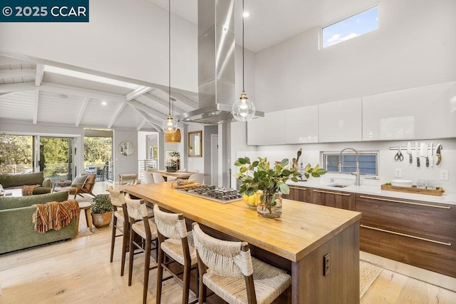 kitchen featuring pendant lighting, high vaulted ceiling, sink, white cabinets, and a center island