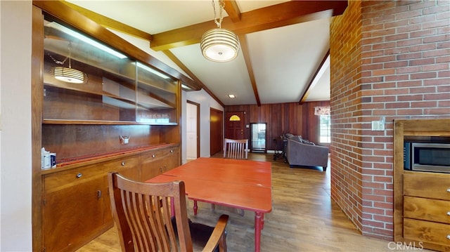 dining space with lofted ceiling with beams, wooden walls, a glass covered fireplace, and wood finished floors