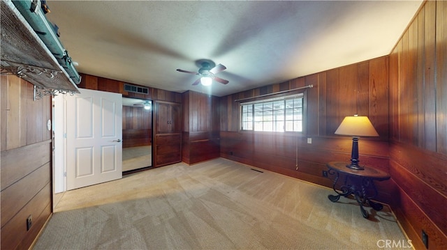 interior space with light carpet, visible vents, ceiling fan, and wooden walls