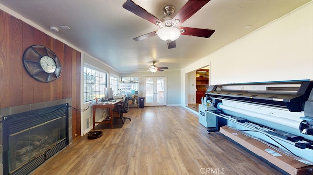 office with wooden walls, a tile fireplace, a ceiling fan, and wood finished floors