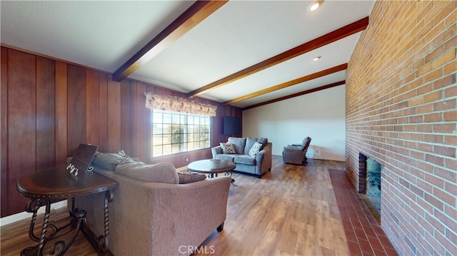 living area with a brick fireplace, brick wall, baseboards, lofted ceiling with beams, and wood finished floors