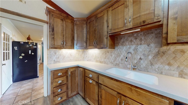 kitchen with a sink, brown cabinets, backsplash, and light countertops