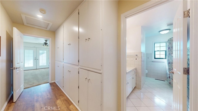 hallway with light tile patterned floors, a wainscoted wall, french doors, and tile walls