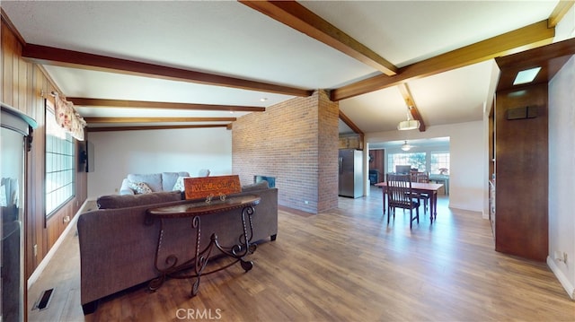 living room with lofted ceiling with beams, a brick fireplace, wood finished floors, and brick wall