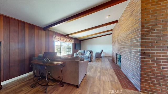 living room with wooden walls, wood finished floors, brick wall, vaulted ceiling with beams, and a fireplace