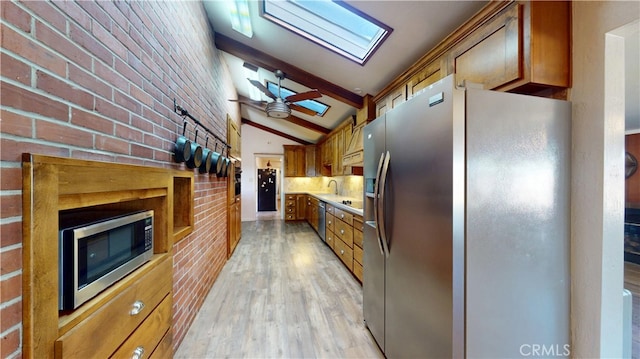 kitchen featuring brick wall, light wood-style flooring, appliances with stainless steel finishes, lofted ceiling with skylight, and brown cabinets