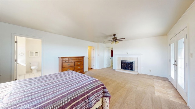 bedroom featuring connected bathroom, light carpet, a fireplace with raised hearth, and a ceiling fan