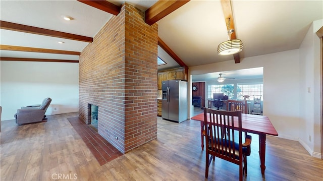 dining area featuring light wood-style floors, a ceiling fan, vaulted ceiling with beams, and a fireplace