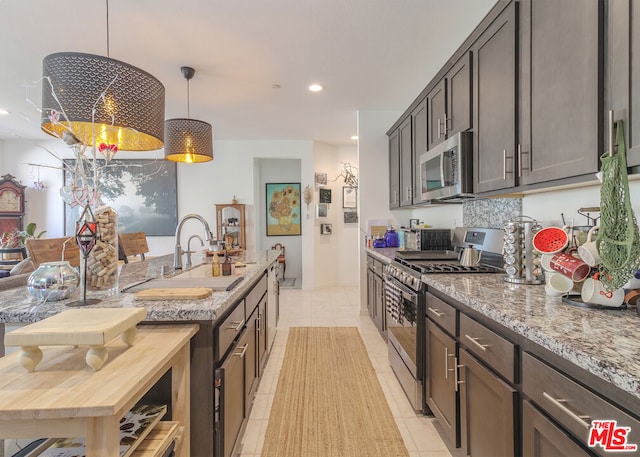 kitchen featuring appliances with stainless steel finishes, decorative light fixtures, light tile patterned floors, dark brown cabinetry, and light stone countertops