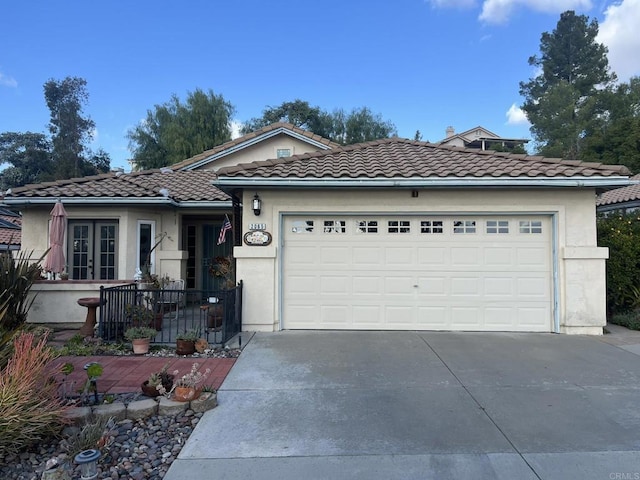 view of front facade with driveway, a tiled roof, an attached garage, french doors, and stucco siding