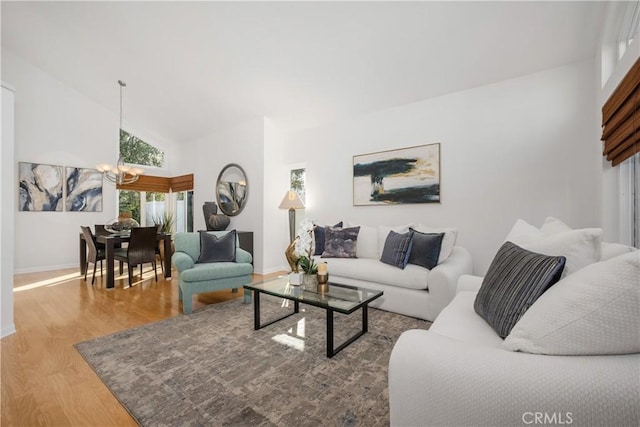 living room with high vaulted ceiling, a notable chandelier, baseboards, and wood finished floors