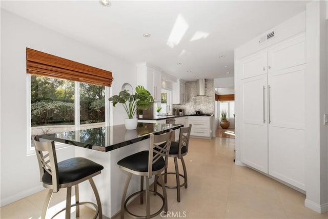 kitchen with dark countertops, wall chimney exhaust hood, plenty of natural light, and decorative backsplash