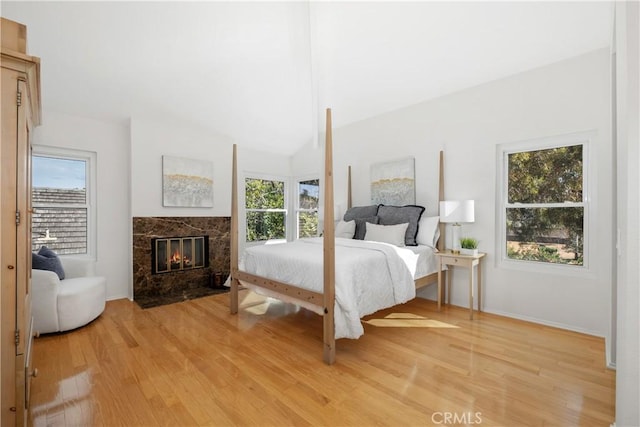 bedroom with a high end fireplace, lofted ceiling, and light wood finished floors