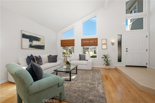 living room with light wood-type flooring, high vaulted ceiling, and baseboards