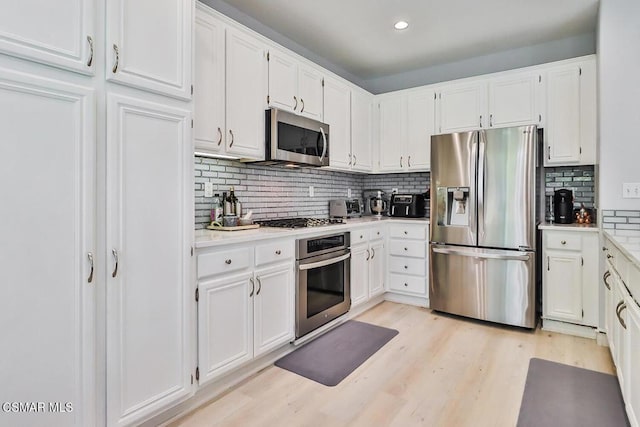 kitchen with stainless steel appliances, white cabinets, and light hardwood / wood-style flooring