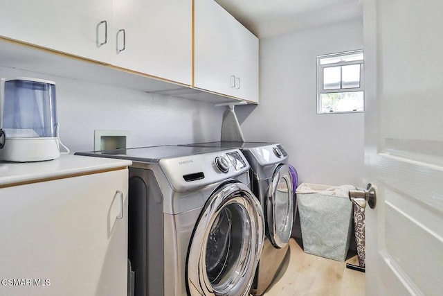 clothes washing area with cabinets, washer and clothes dryer, and light hardwood / wood-style flooring