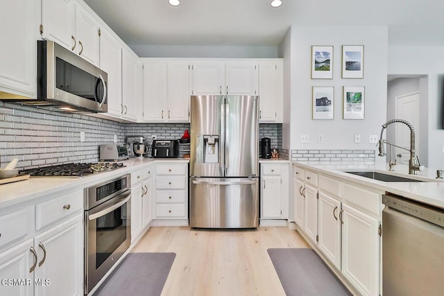 kitchen with appliances with stainless steel finishes, tasteful backsplash, sink, white cabinets, and light wood-type flooring