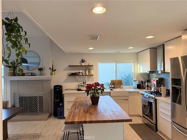 kitchen featuring butcher block countertops, wall chimney range hood, stainless steel appliances, tasteful backsplash, and a kitchen island