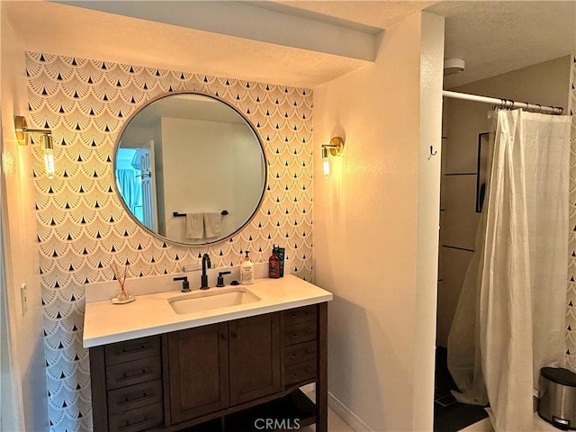 bathroom with a shower with curtain, a textured ceiling, wallpapered walls, baseboards, and vanity