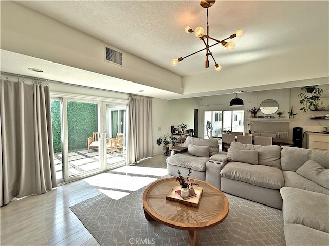 living area with an inviting chandelier, light wood-style floors, visible vents, and a textured ceiling