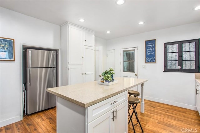 kitchen with hardwood / wood-style floors, stainless steel refrigerator, a breakfast bar area, white cabinets, and a center island