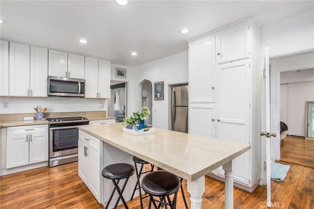 kitchen featuring stainless steel appliances, white cabinetry, a kitchen bar, and light hardwood / wood-style floors