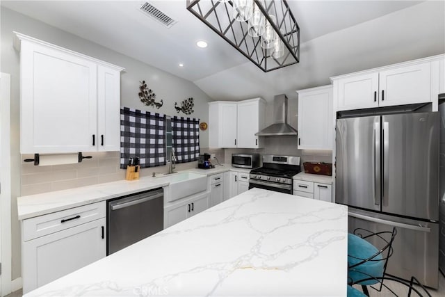 kitchen with appliances with stainless steel finishes, white cabinets, decorative light fixtures, and wall chimney exhaust hood