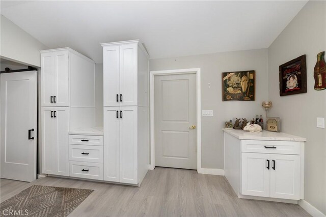 interior space featuring a barn door, white cabinetry, light countertops, and light wood-style flooring