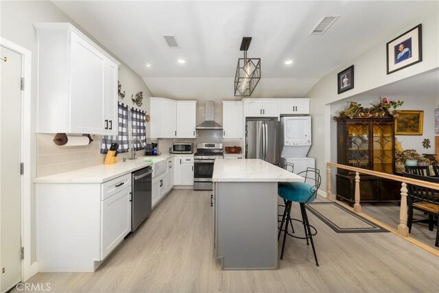 kitchen with white cabinets, a center island, hanging light fixtures, stainless steel appliances, and wall chimney range hood