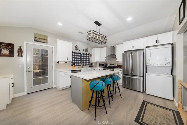 kitchen featuring wall chimney exhaust hood, appliances with stainless steel finishes, hanging light fixtures, and white cabinetry