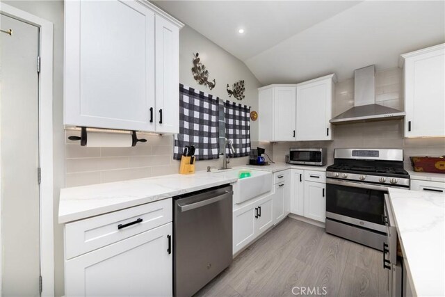 kitchen with backsplash, appliances with stainless steel finishes, white cabinets, a sink, and wall chimney exhaust hood