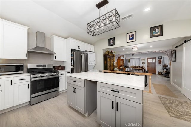 kitchen featuring stainless steel appliances, a kitchen island, white cabinets, hanging light fixtures, and wall chimney exhaust hood