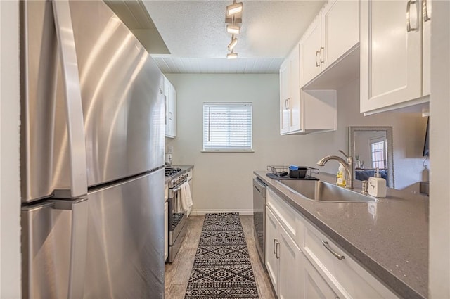 kitchen with white cabinetry, sink, dark stone counters, stainless steel appliances, and track lighting