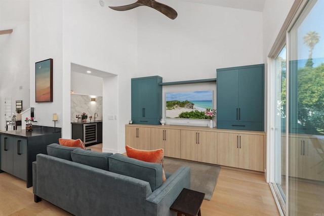 living room with a towering ceiling, beverage cooler, ceiling fan, and light wood-type flooring