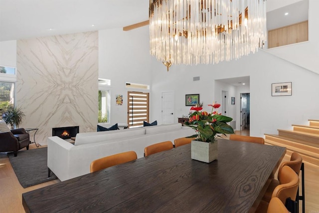 dining area with hardwood / wood-style flooring, a towering ceiling, a chandelier, and a high end fireplace