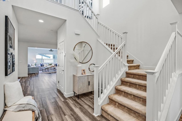 staircase featuring wood-type flooring, ceiling fan, and a high ceiling