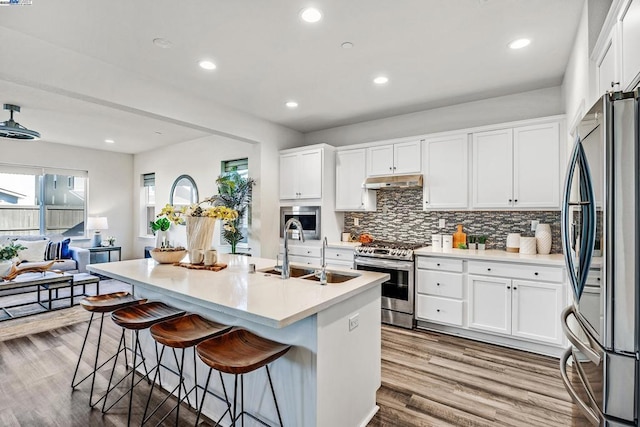 kitchen with a breakfast bar, sink, white cabinetry, stainless steel appliances, and a kitchen island with sink